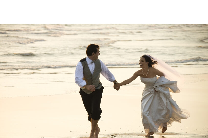 groom and bride running happily on the beach