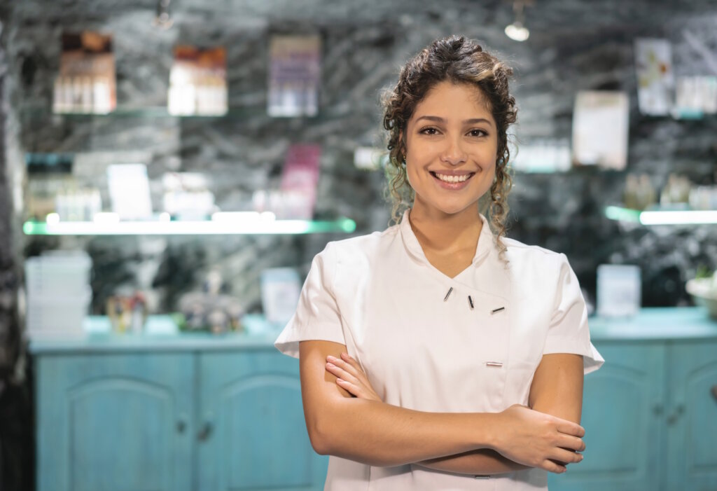 Portrait of a happy beautician selling beauty products at the spa and looking at the camera smiling