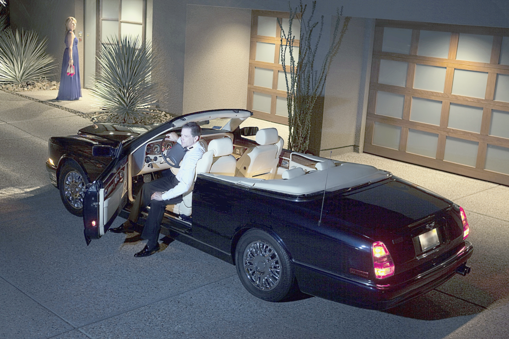 Attractive affluent couple. Husbank is in a fancy convertiable and the wife is holding a glass and her shoes waiting to go into a luxury home