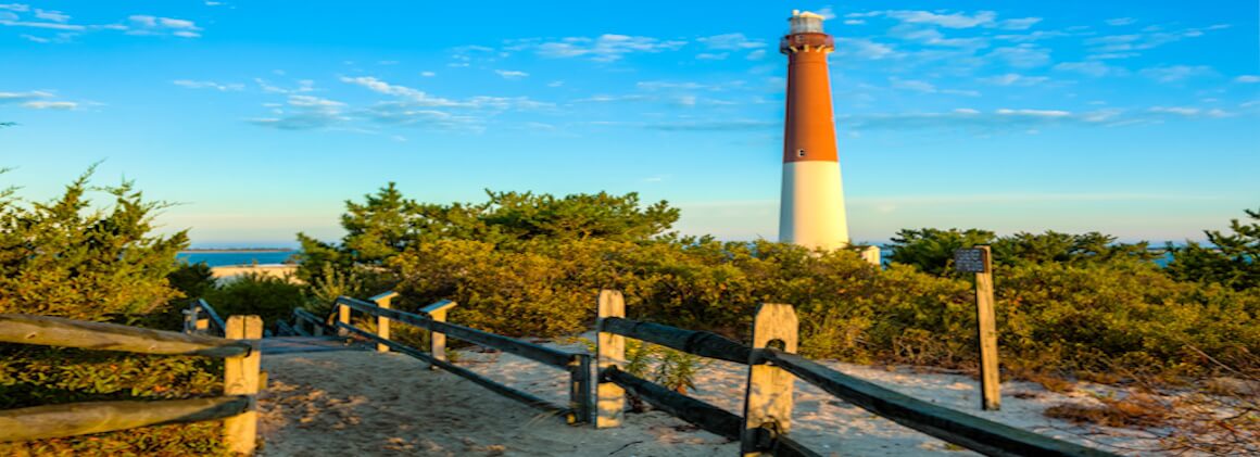 The Barnegat Lighthouse, also known as Old Barney, is located at Barnegat Light, New Jersey. A split rail fence guides the way along a sandy path to the 40-foot-tall red and white lighthouse which is accessible to tourists willing to climb its 217 steps.